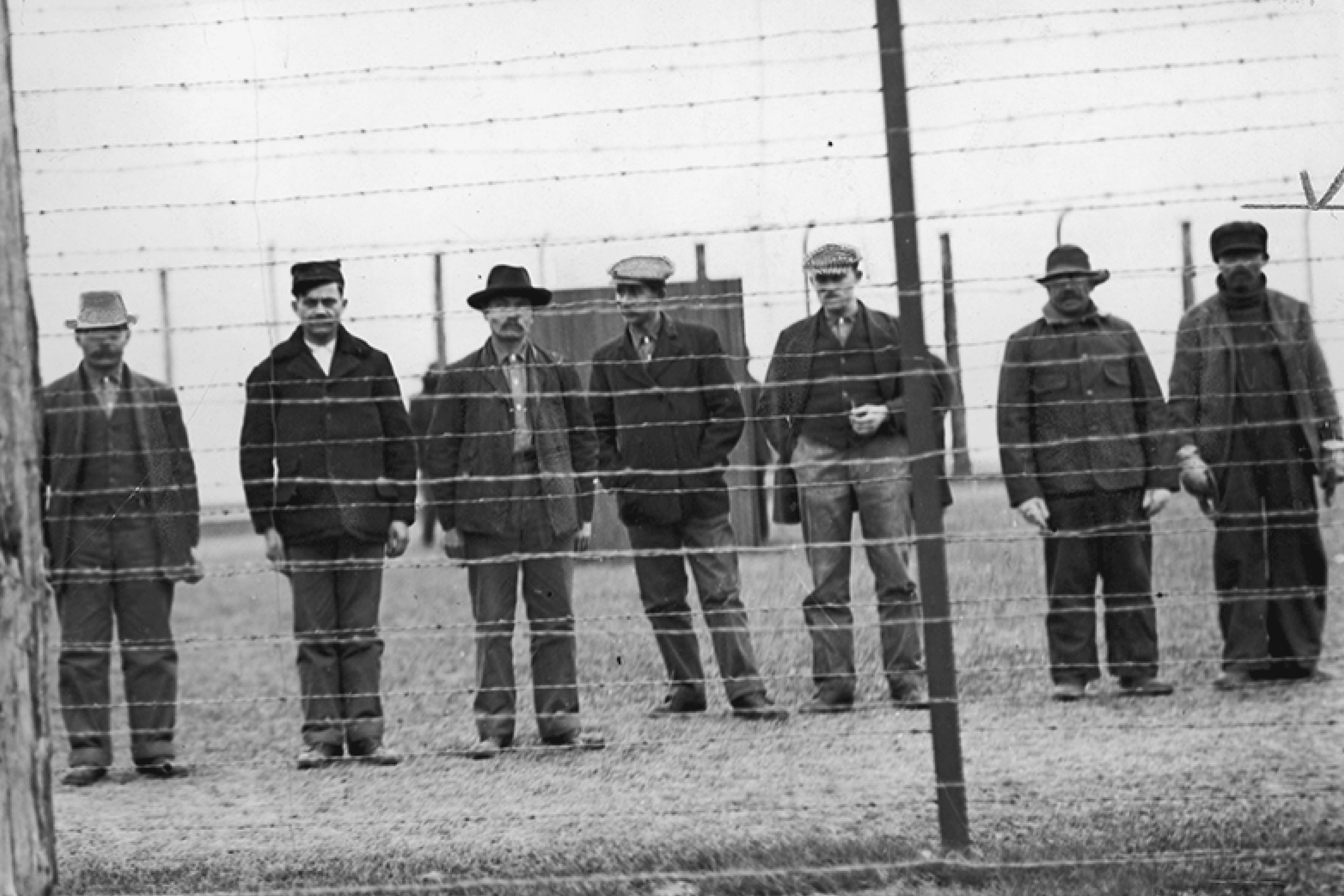 Interned men behind barbed wire at a camp in Canada, circa 1914–1920.